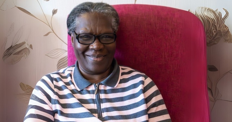 Smiling older woman in glasses and a striped shirt sitting in a red chair.