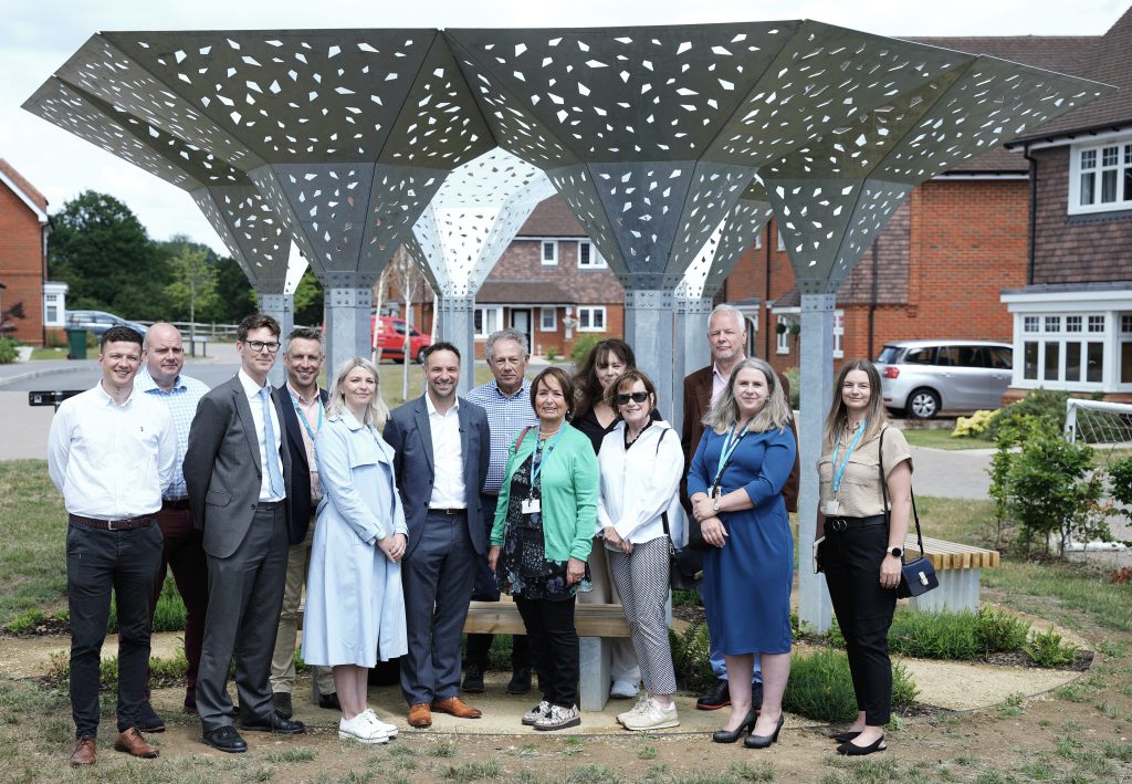 A photo of attendees at the Loxwood Rural Housing Report Launch. Attendees are stood for a group photo, mostly smiling directly into the camera under a canopy in front of the Loxwood housing scheme. (L-R) Nick Keyden, PR & Media Manager; Rob Boughton, CEO of Thakeham; Alistair Smyth, Director of Policy and Research at the NHF; Jonathan Lazell, Stonewater CEO, Aileen; James Bradbury, Group Director for Growth and Development; Sheila Collins, Stonewater Chairman; Jane Scott, Board Member; Jennifer Bennet, Board Member; UoL member (can’t remember his name!); Marie Riordan, Director of Development; Gemma McCartney, Development Manager.