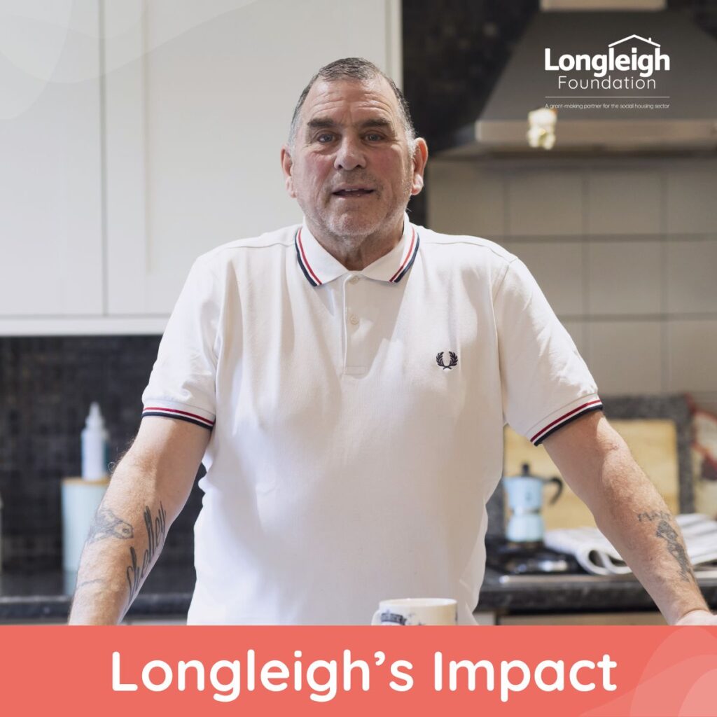 A man stands at a kitchen counter, facing the camera, dressed in a white collared shirt with a small logo. Behind him is a tidy kitchen setting. The Longleigh Foundation branding and the phrase "Longleigh’s Impact" frame the image, suggesting a story of positive transformation.