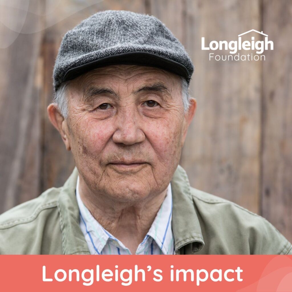 An older man wearing a gray flat cap and light green jacket looks calmly at the camera, standing in front of a wooden background. The image includes the Longleigh Foundation logo in the top right corner and the text “Longleigh’s impact” along the bottom on an orange banner.