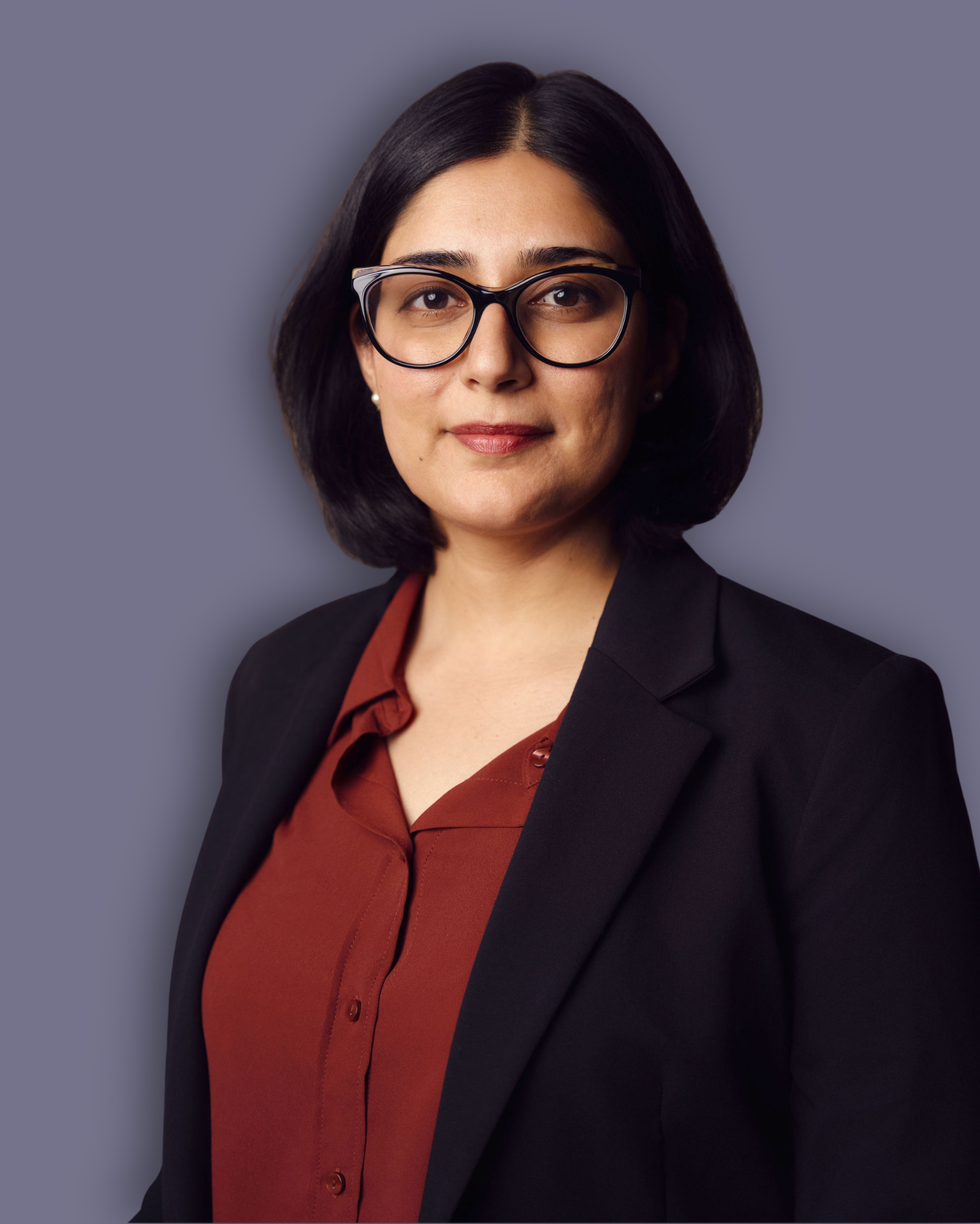 A headshot photo of Nayan Nath wearing a black blazer and burgundy shirt, a Longleigh Trustee on a lilac background.