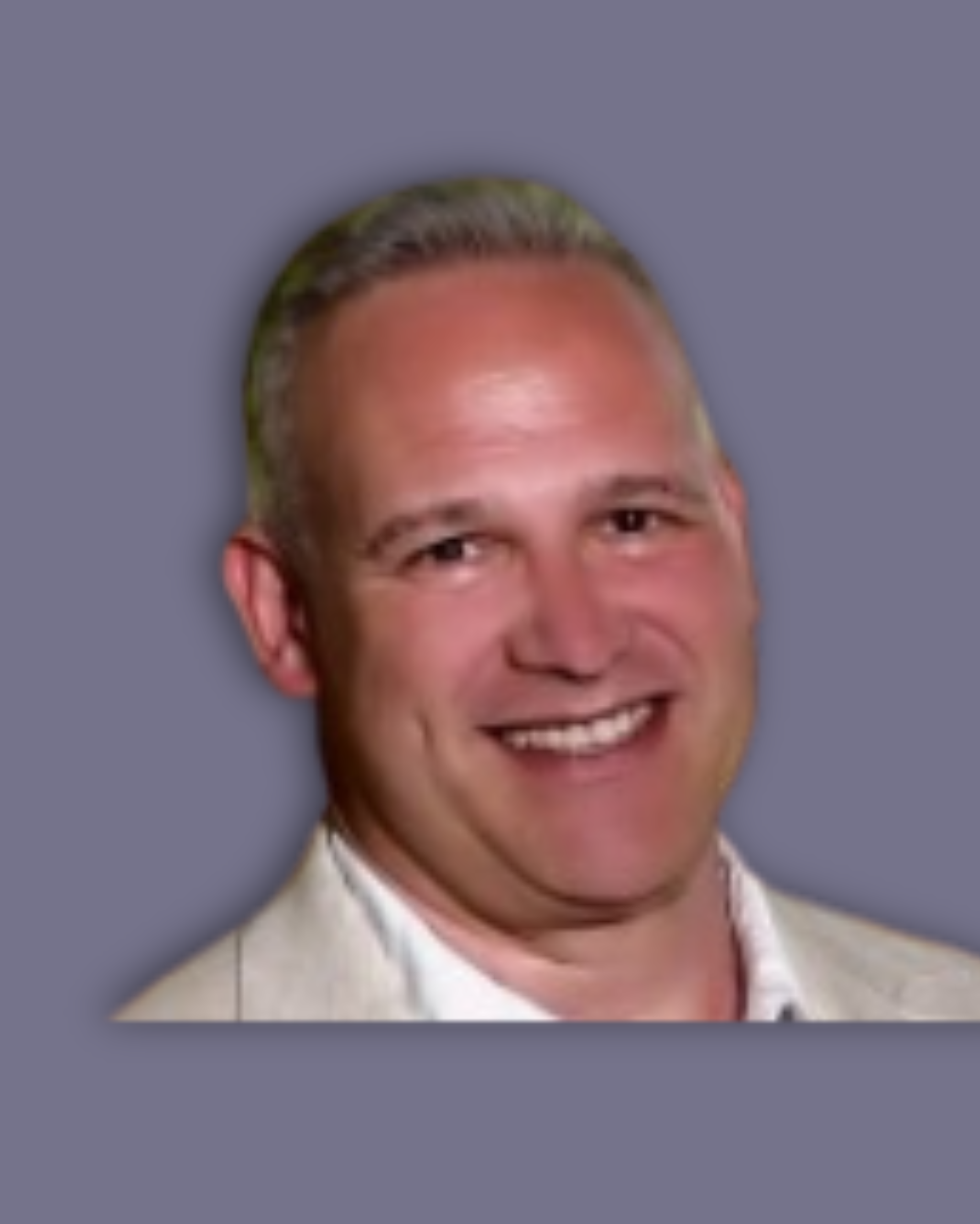 Richard Lakey, smiling directly the camera wearing a beige suit jacket and white shirt.