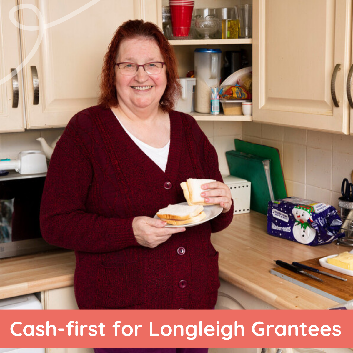 A smiling woman is standing in a kitchen holding a plate with a sandwich and toast. She is wearing a burgundy cardigan, and the countertop behind her has kitchen items including utensils, a butter dish, and packaged bread. A banner at the bottom reads “Cash-first for Longleigh Grantees.”