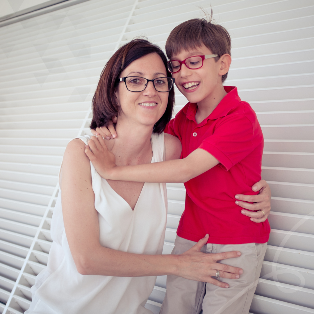 A child held close by his mother in front of white window blinds, with the child’s arms around his mother, symbolising a family gaining the freedom and support needed for safe travel.